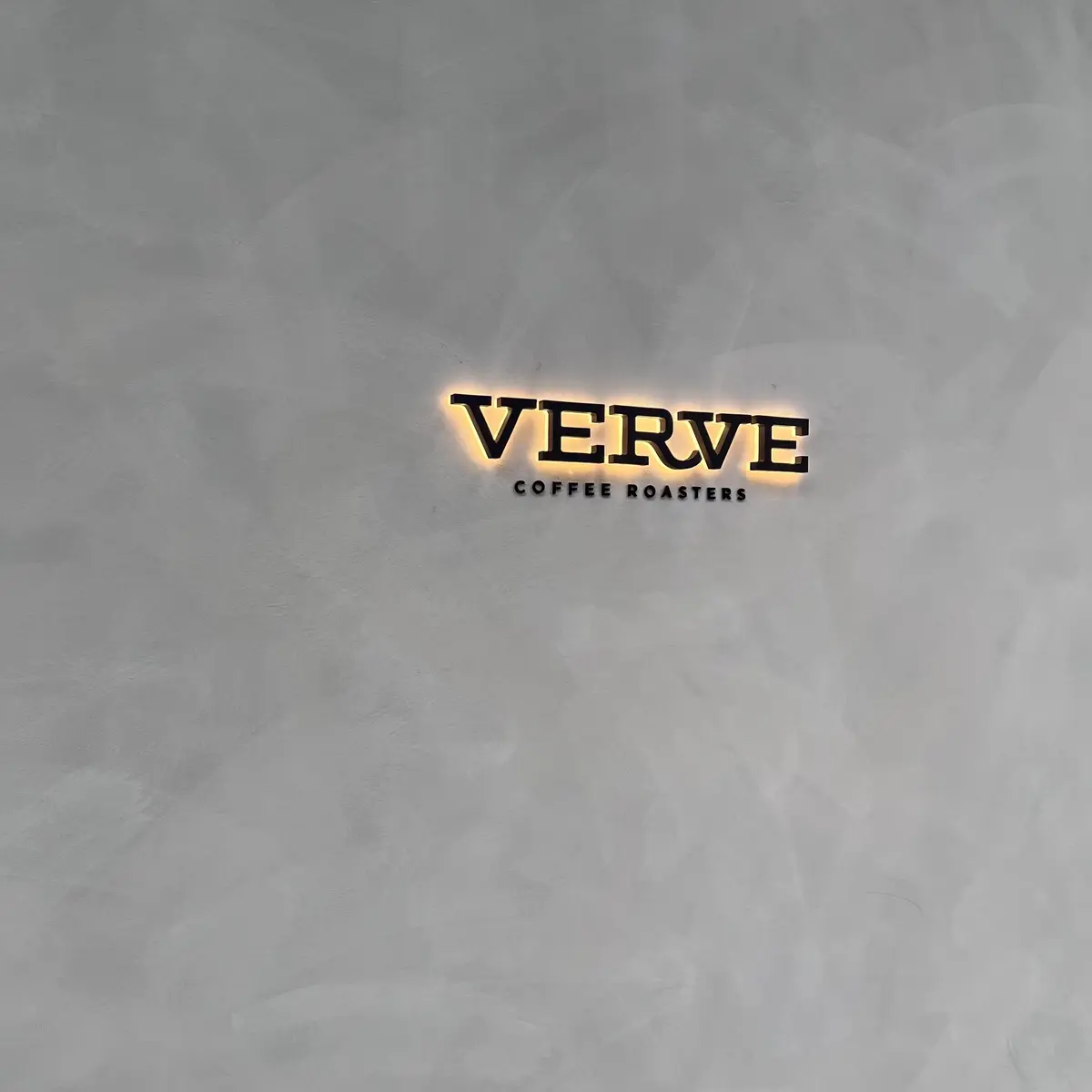 灰色の壁に設置された、黒い文字で「VERVE COFFEE ROASTERS」と書かれたロゴ。