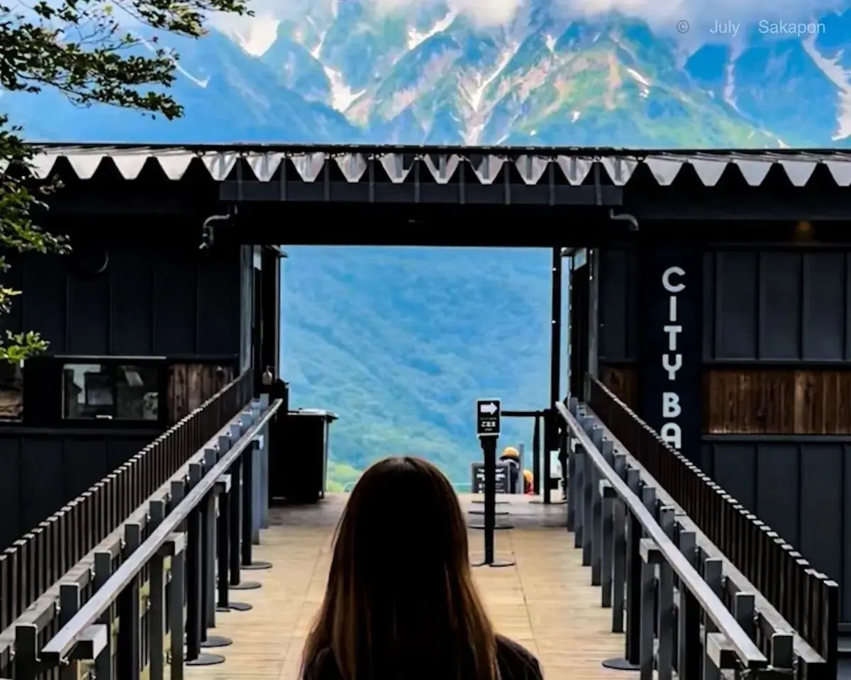 屋根付きの橋に立つ女性。手すりを背に、遠くの山々を眺めている。橋には「CITY BAR」の文字が縦に書かれている。背景は霧に包まれた山々。