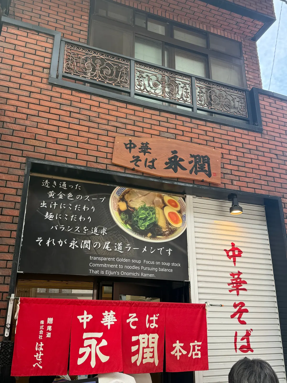 レンガ造りの2階建ての建物正面。黒板にラーメンのイラストとメニュー、赤い看板に「中華そば 永剛 本店」の文字。窓の上には装飾的なデザイン。尾道で、尾道グルメの尾道ラーメン。中華そば、永潤本店。
