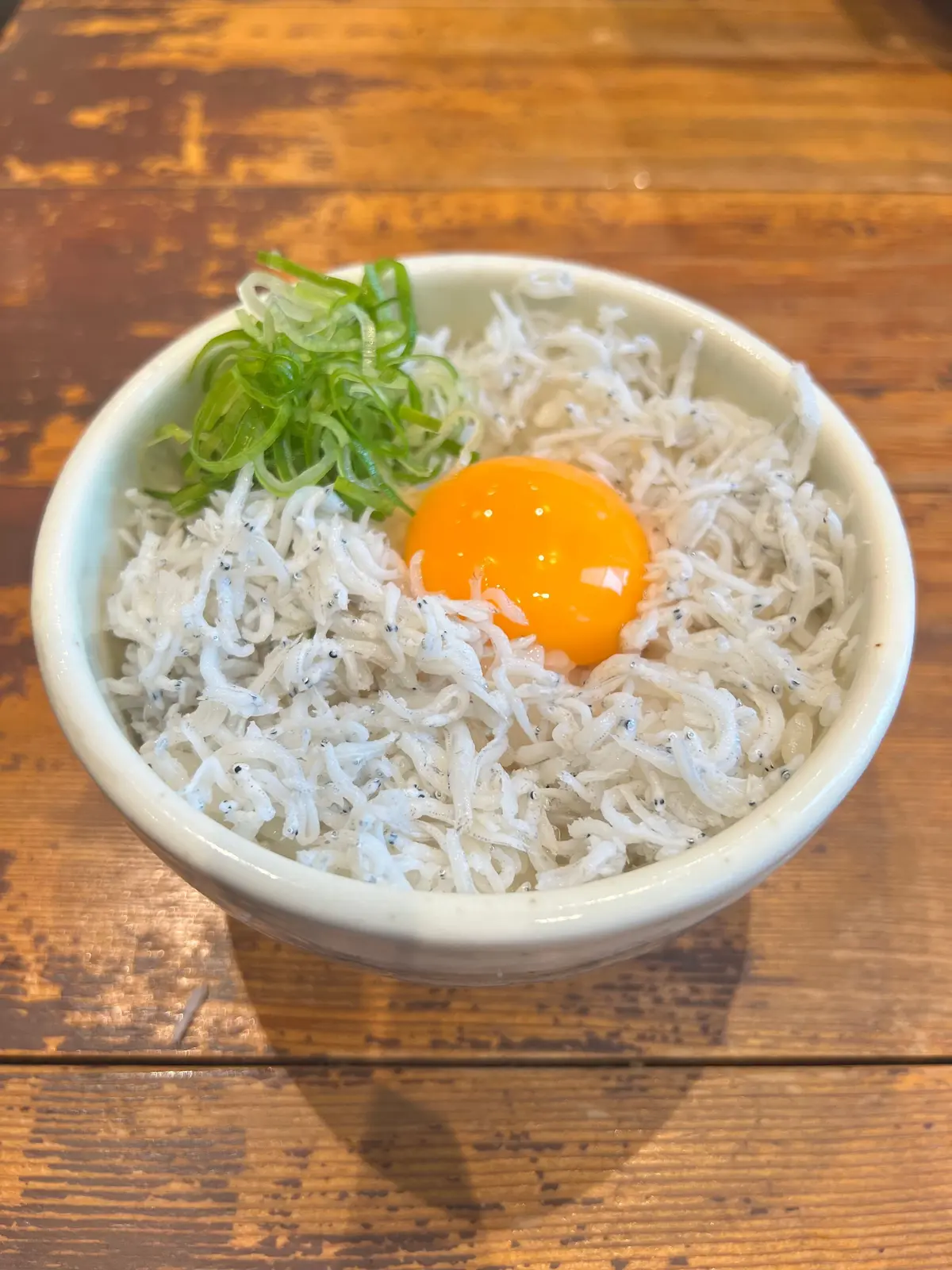 しらすご飯。黄身の卵が乗せられ、緑のネギが添えられている。