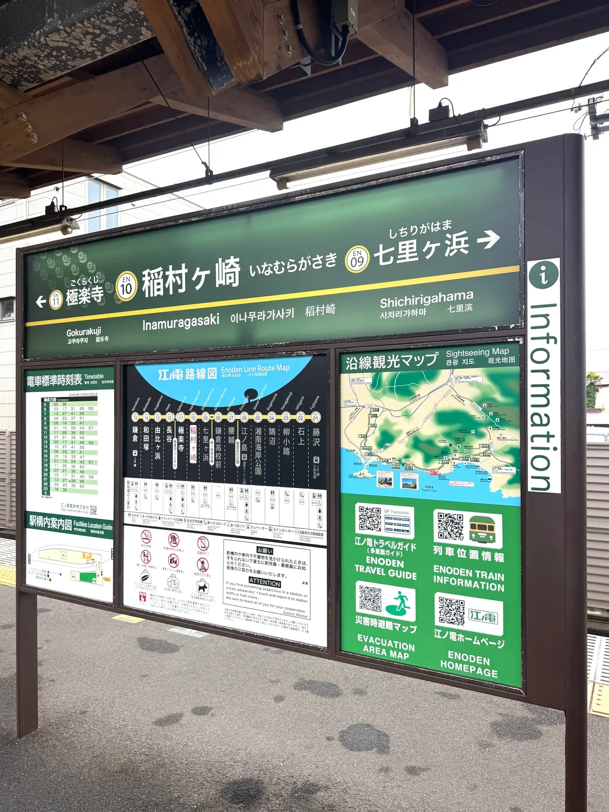 稲村ヶ崎駅に設置された緑色の案内板で、左から「時刻表」「路線図」「観光マップ」「避難地域マップ」が表示されている。