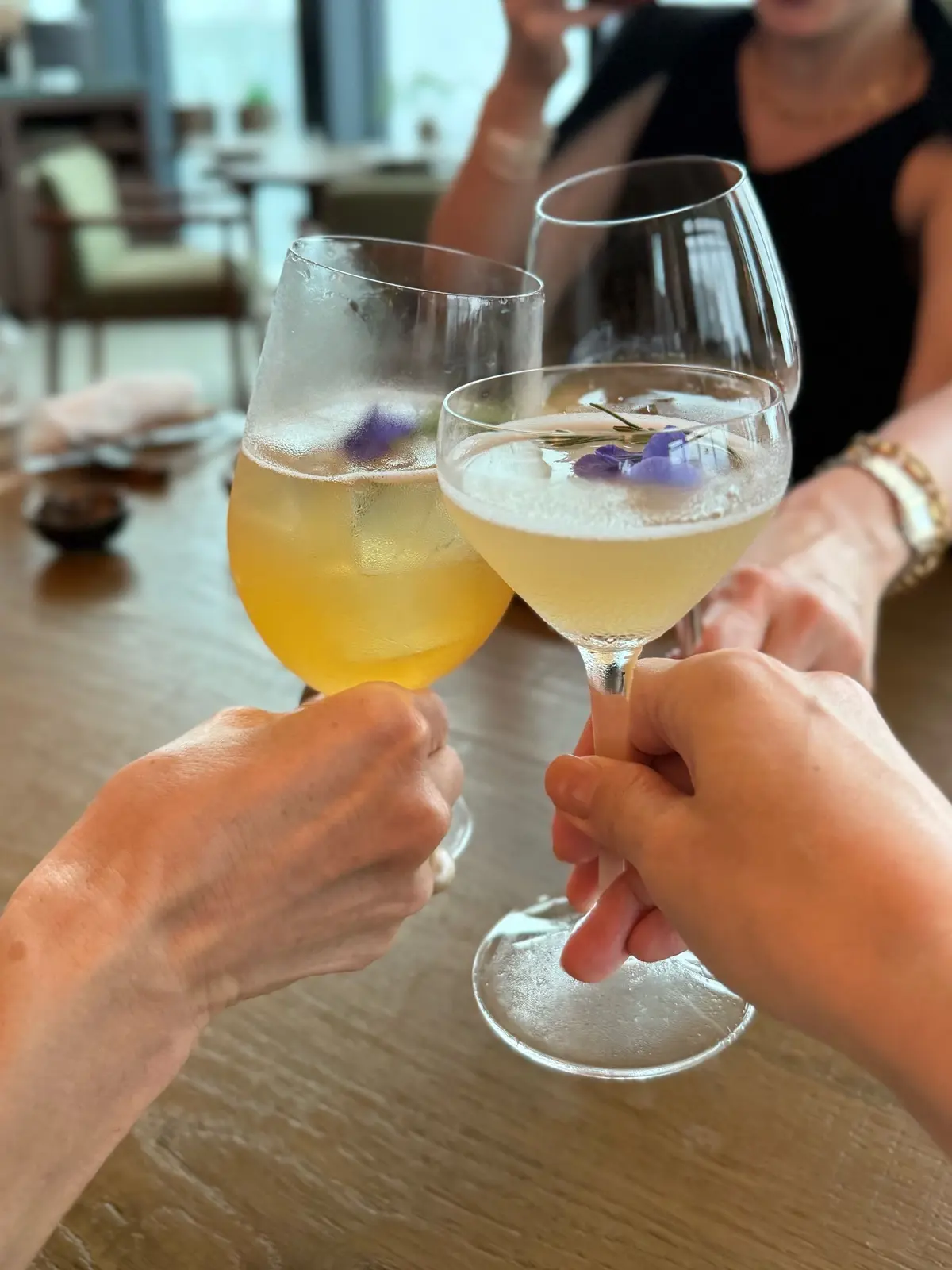 １Hotel Tokyo ３８階　レストラン「NiNi」、二人の手でクラシックなワイングラスに、氷と紫の花が浮かぶ黄色のカクテルが掲げられている