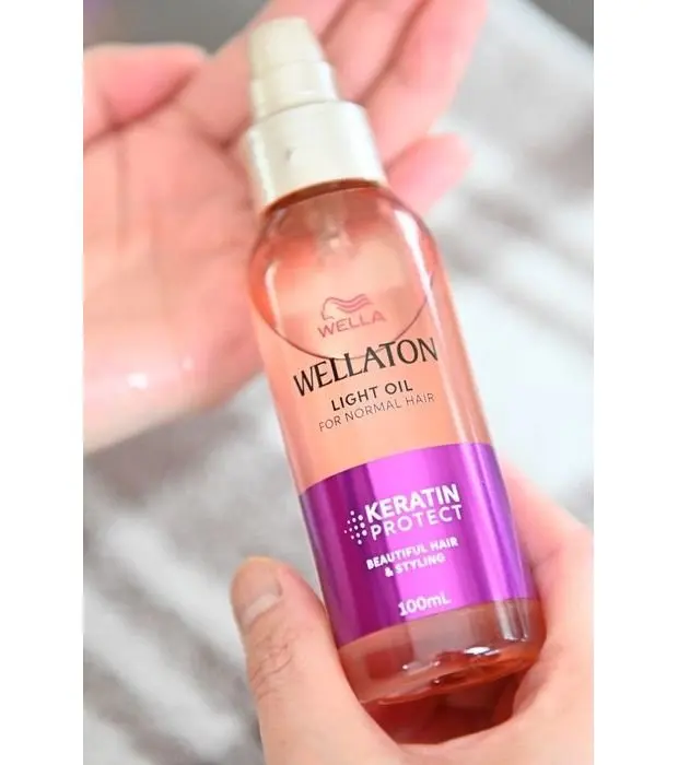 手で保持された、ウェラ（Wella）の「Wellaton ライトオイル」ボトル。ピンク色のボトルに、紫色のラベルが貼られており、「ケラチンプロテクト」の文字が記載されている。容量は100ml。