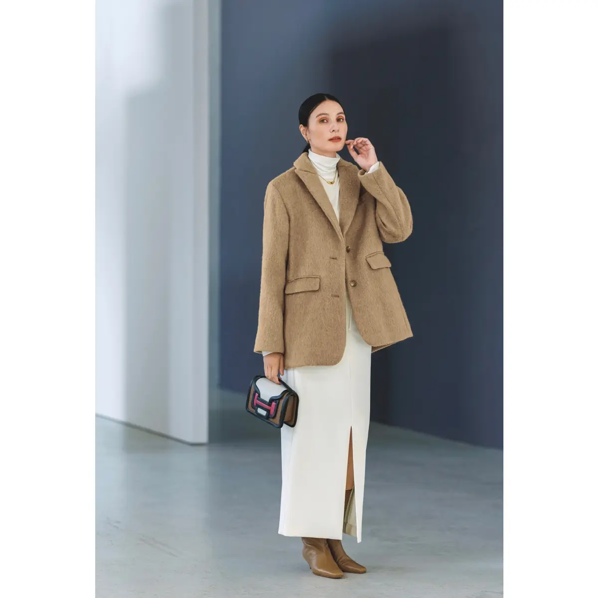 白のタートルネックトップスに白ロングスカートを合わせ、キャメルのテーラードスタイルのジャケットコートをはおったコーディネート　モデル・田沢美亜　
