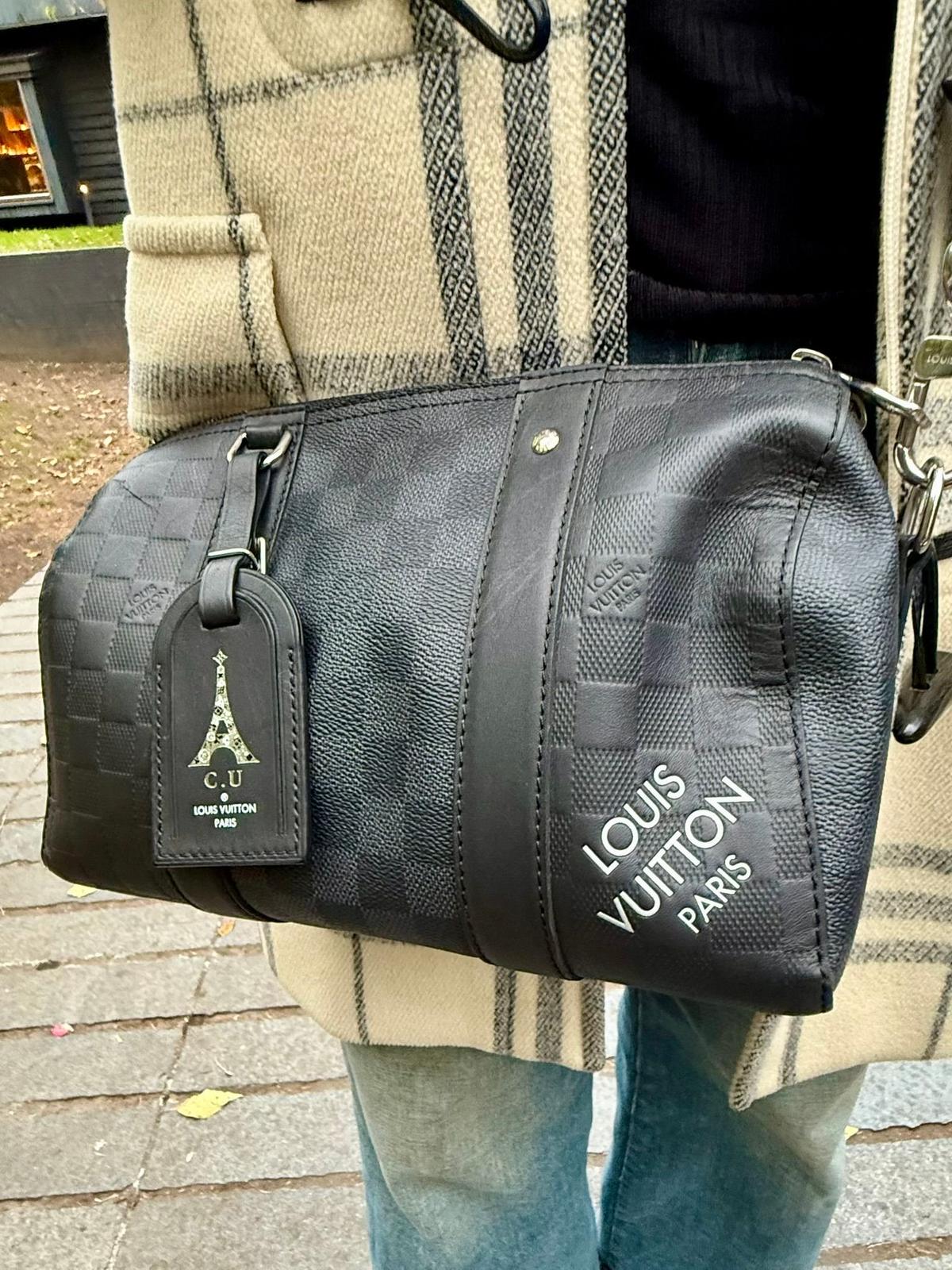 ルイ・ヴィトン製のグレーのショルダーバッグ。中央に大きく「LOUIS VUITTON PARIS」のロゴが刻印されている。バッグにはタグが取り付けられており、エッフェル塔のイラストが描かれている。