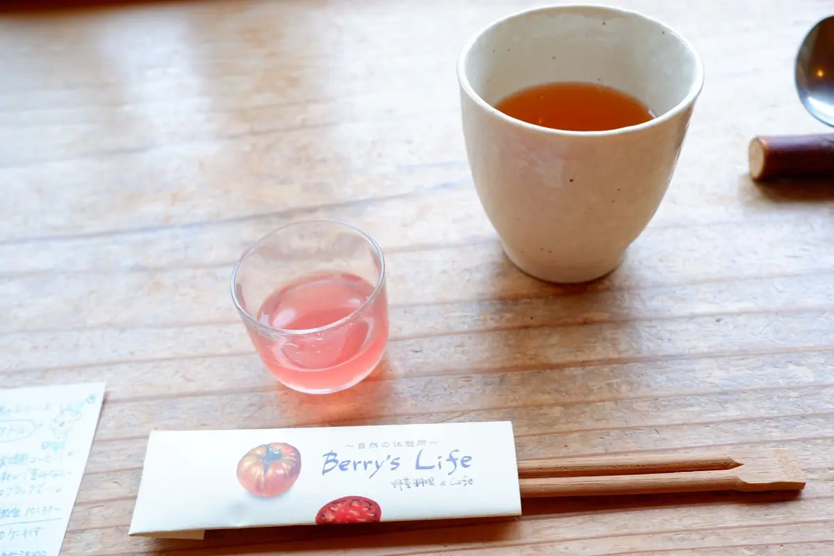 木製のテーブルに置かれた、Berry's Lifeのロゴ入りの白い袋と、飲み物が入ったグラス、湯呑み。グラスにはピンク色の液体、湯呑みには茶色の液体が入っている。
