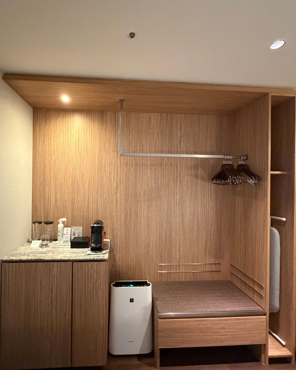 ホテルの洗面台横に設置されたキャビネット。シャンプー、コンディショナー、ネスプレッソのコーヒーメーカー、マグカップが置かれている。背景には木目調の壁。