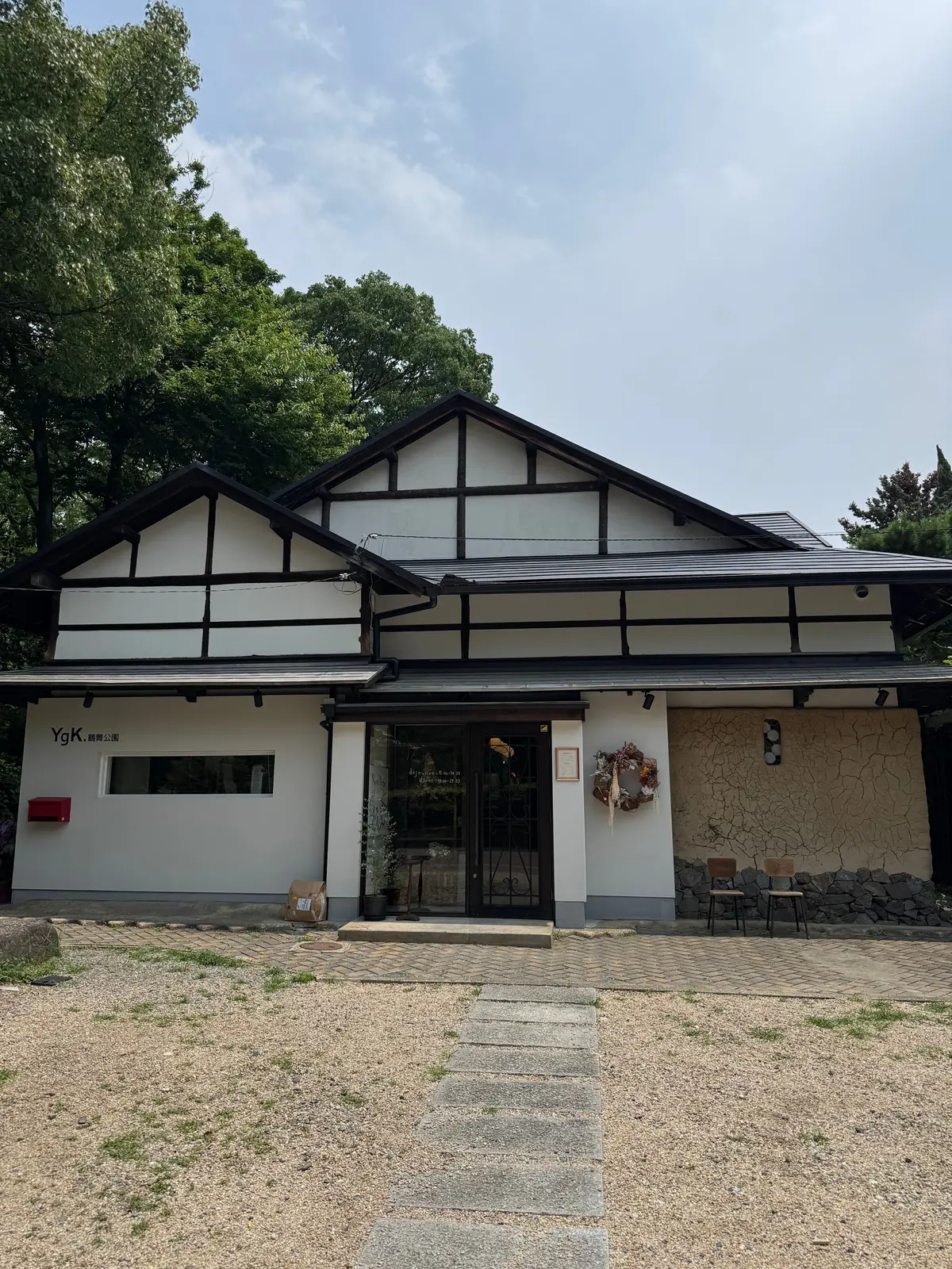 白と黒の和風建築の建物で、玄関には花輪が飾られ、左右に椅子が置かれている。