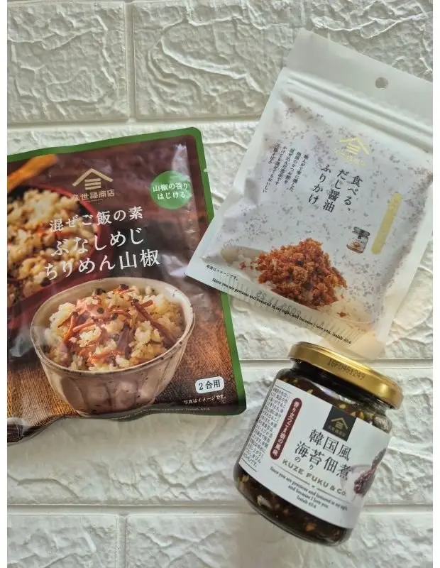 木枯らし紋次郎の「深ぜご飯の素 ぶりめん山椒」2個、「食べるだし醤油 かりかり」、「韓国風海苔佃煮」の3点が、白いドット柄の布の上に置かれている写真。ご飯に混ぜた様子がパッケージに描かれている。