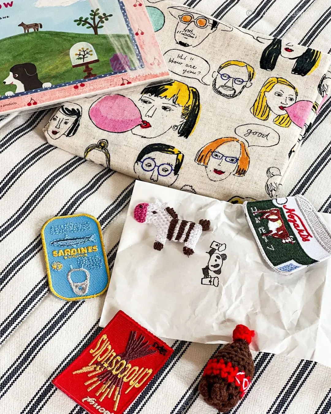 手作りの小物やパッチが並ぶ布地と刺繍パッチのセット。手編みの動物フィギュア、漫画風のキャラクターが描かれた布地、ブランドロゴの刺繍パッチが混在している。