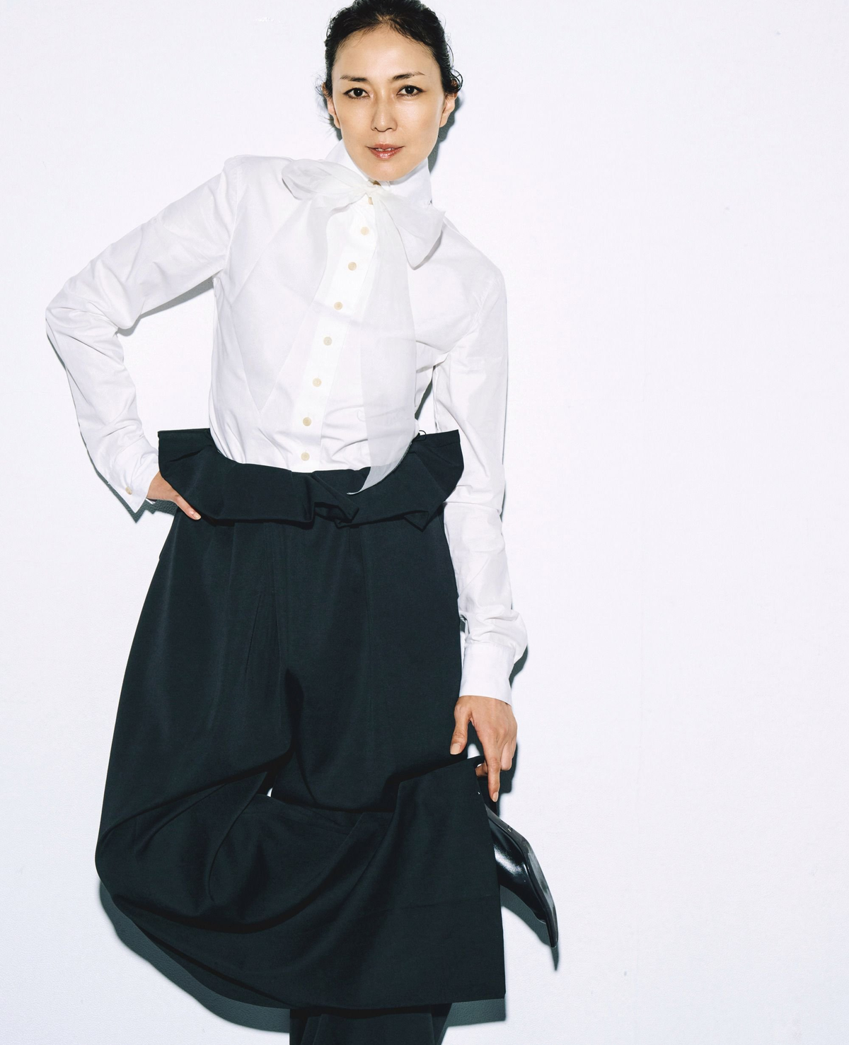 大人がケイトにときめく理由【板谷由夏×伊藤美佐季 私を輝かせる「新ブランド考」】白い襟のシャツに黒いスカートを着用した女性。右手を腰に当て、左手でスカートを持ち、やや斜めのポーズ。背景は白。
