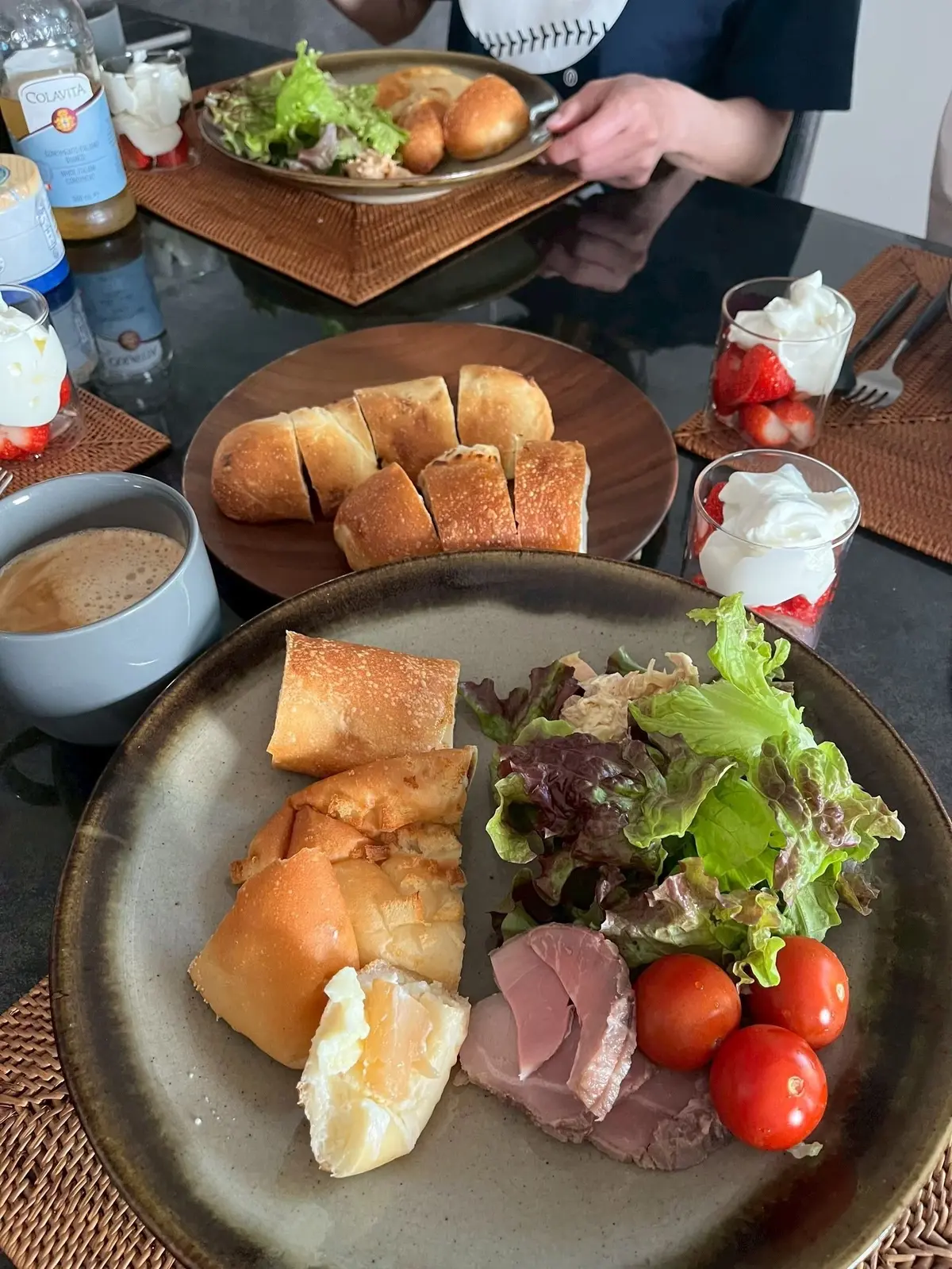 サンドイッチ、トマト、チーズ、葉物野菜が並ぶプレートと、パンとサラダのプレートがテーブルに置かれている