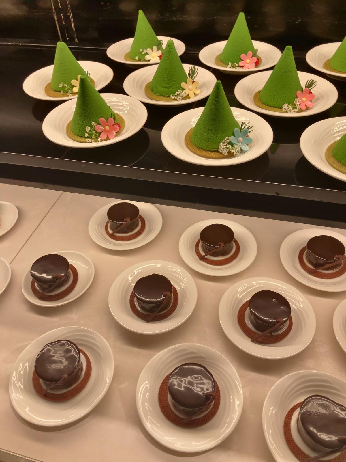 緑のモンブランとチョコレートケーキが白いプレートに並ぶ、華やかなデザートのディスプレイ