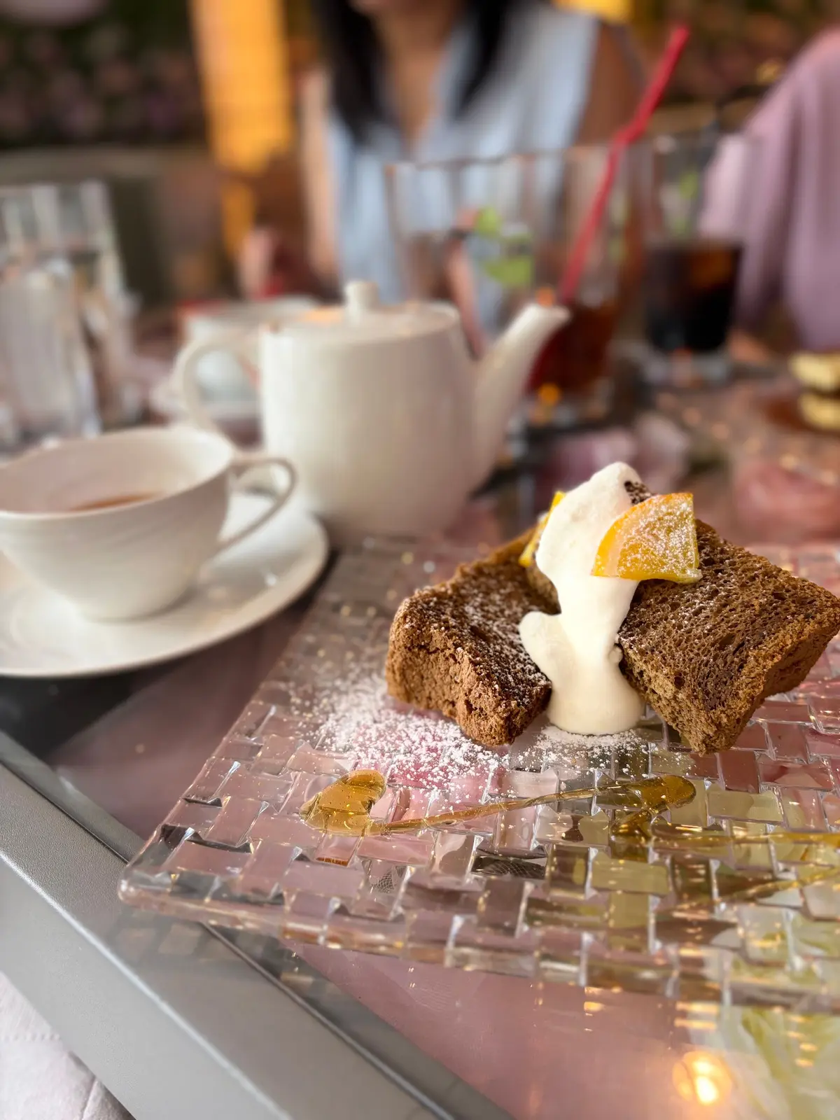 ほうじ茶のシフォンケーキにクリームとオレンジスライスをトッピングしたデザートが透明なプレートに置かれ、隣には白いティーカップとティーポットが並んでいる