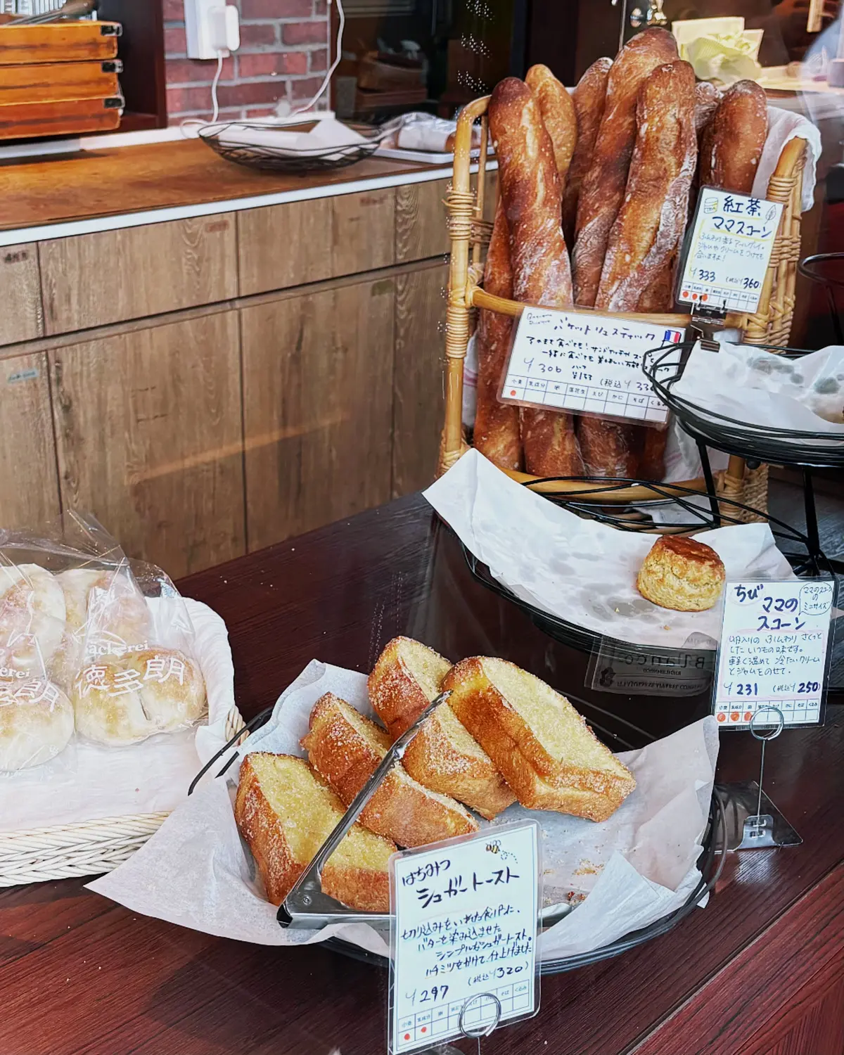 パンとペイストリーが並ぶ店内のディスプレイ。ワゴンの上にベーグルとバゲットが並び、切り分けたパンのプレートと価格表示カードが置かれている。