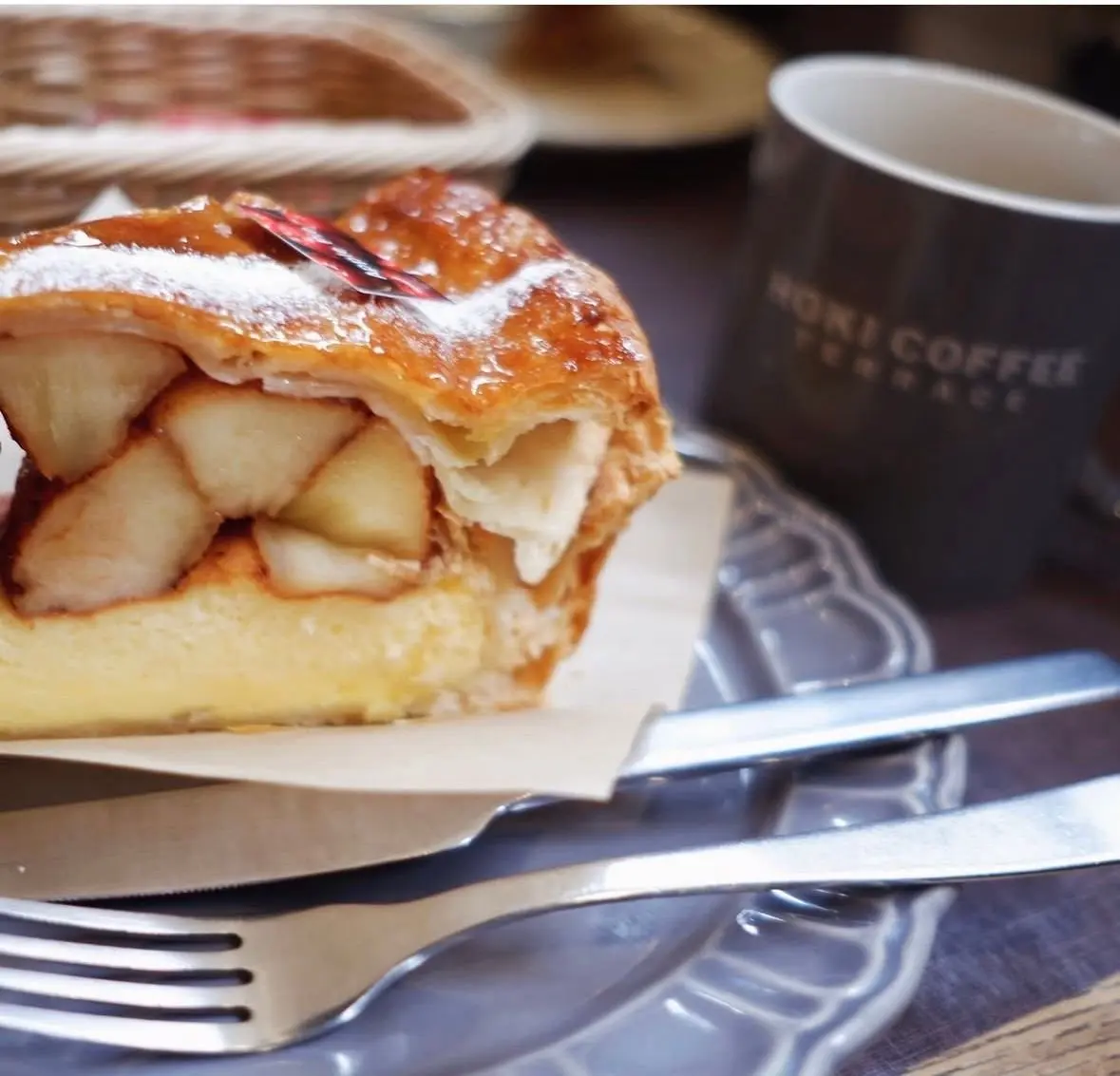 アップルパイの一切れが皿に載せられ、フォークとナイフが添えられています。背景には「HOKI COFFEE TERRACE」と書かれたコーヒーカップがあります。