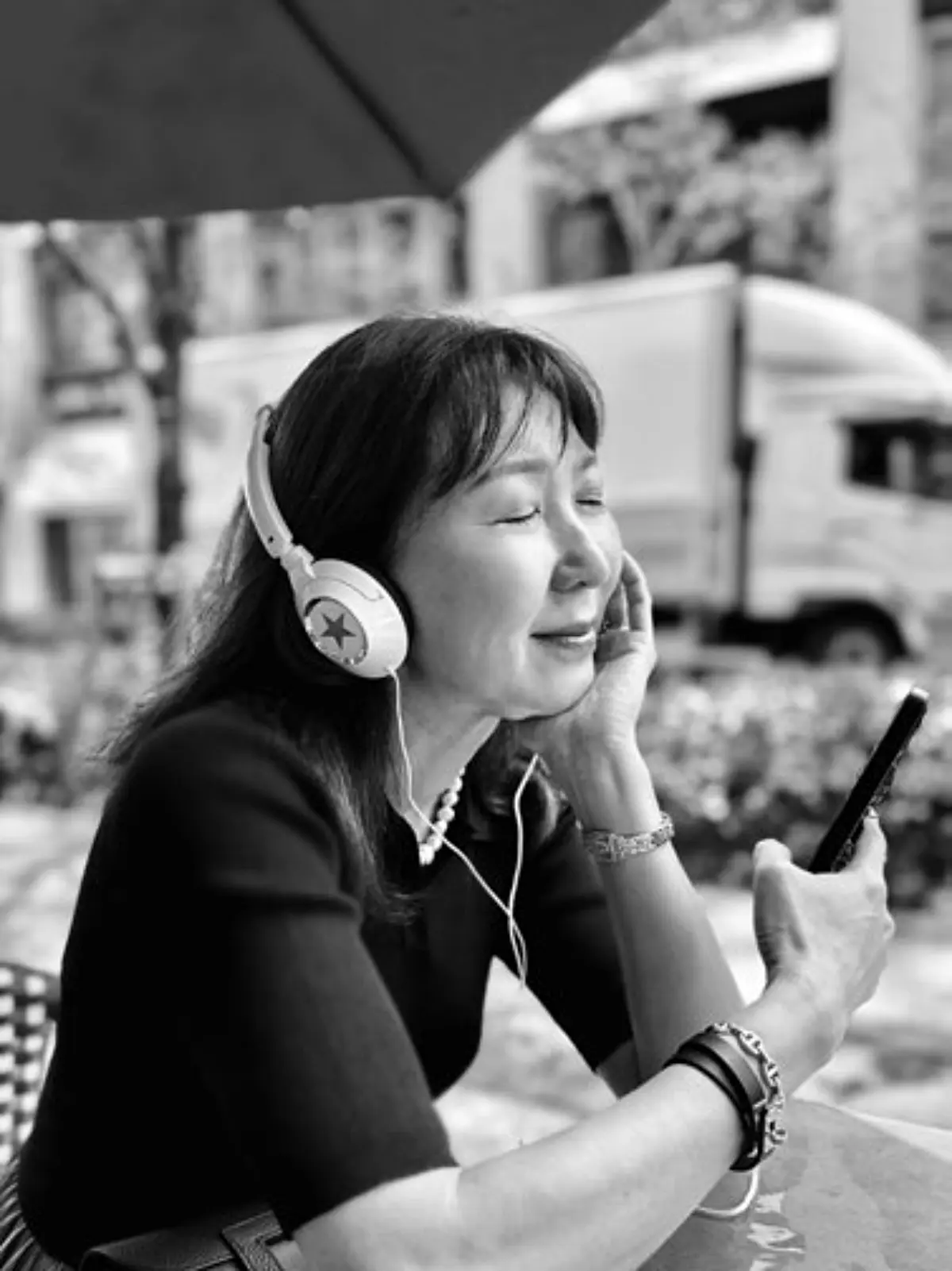 自律神経の整え方　女性が屋外でイヤホンを装着し、スマートフォンを見ながらリラックスしている。背景には建物とトラックが見える。
