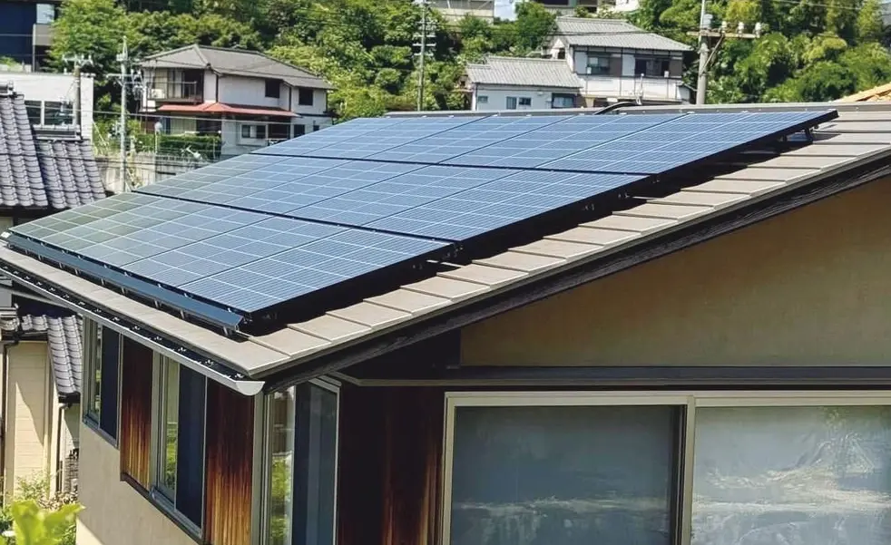 屋根にソーラーパネルが設置された住宅。周囲には緑豊かな住宅街が広がり、青空に白い雲が浮かんでいる。