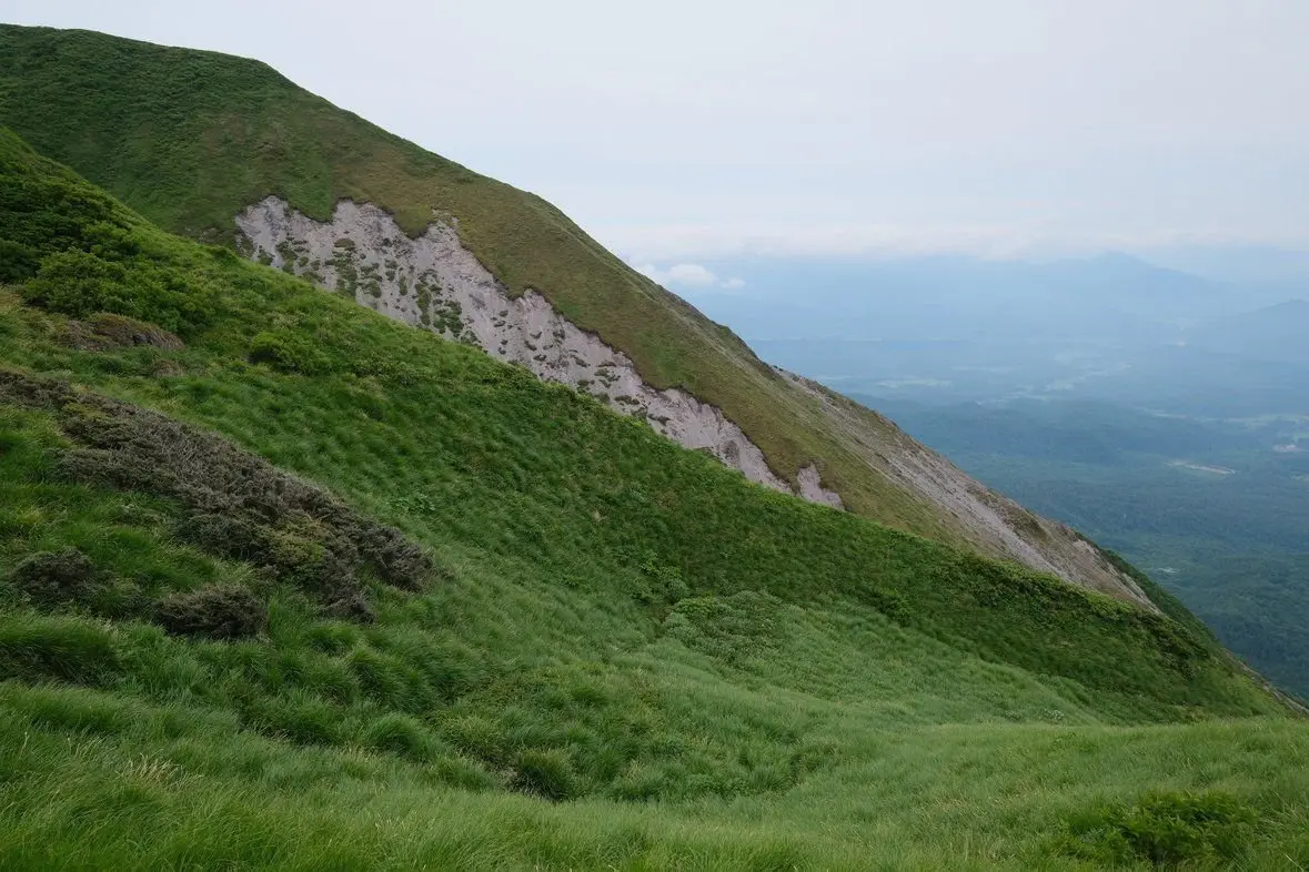 緑豊かな山腹の斜面、遠くに広がる山並みと谷が広がる風景
