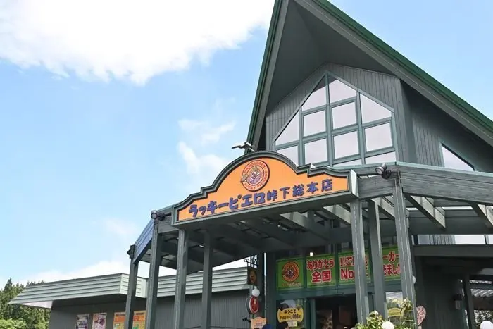 木造建築の建物正面。屋根は緑色の縁取りで、大きな窓が並ぶ。看板には「ラッキーピエロ 下総本店」の文字とロゴマークが掲示されている。