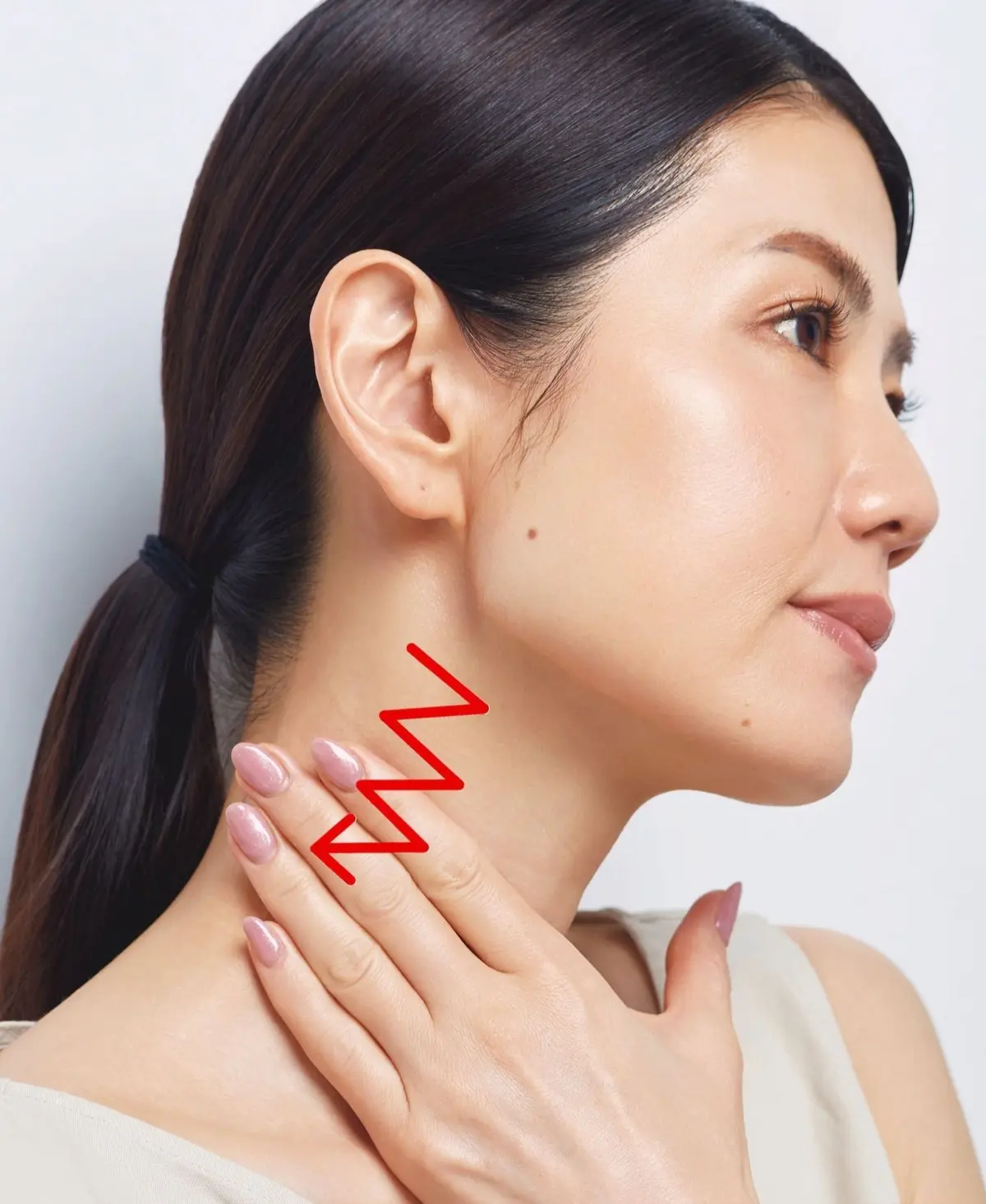 若いアジア系の女性が、首筋に手を当てている横顔。黒髪を後ろでまとめ、ベージュの服を着ている。赤色の矢印が首筋を指している。