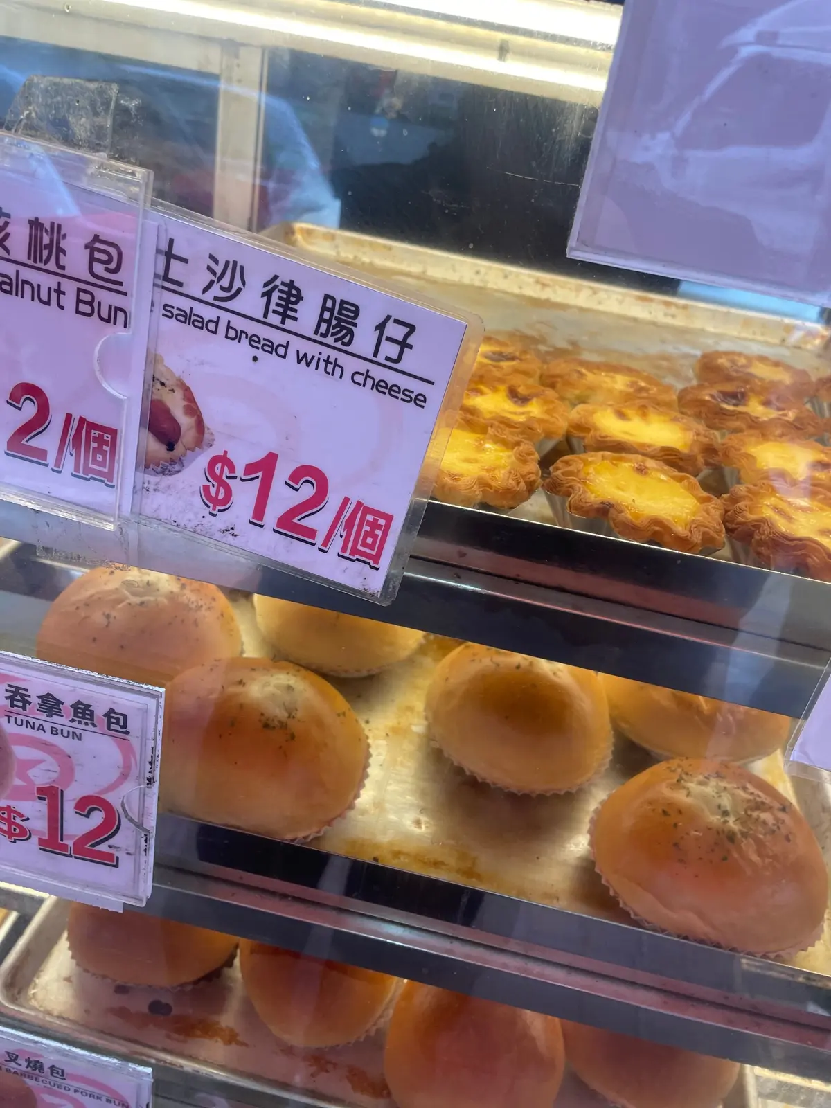 ガラスケースには、チーズ入りサラダブレッドとナッツパンが並び、価格と数量の表示があります。下段には、マグロ入りパンが複数並んでいます。