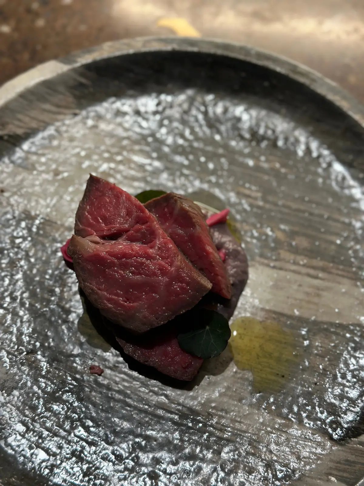 銀色の器に盛り付けられた、赤紫色の肉料理。表面は軽く焼き色が付いており、葉やピンク色の飾り付けが添えられている。