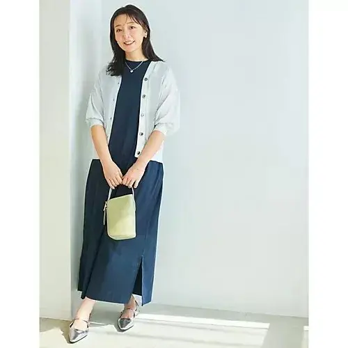 グレーのフレンチスリーブワンピースを着た女性が、黒の小物とサンダルを身につけ、左手で黒のクラッチバッグを持っている