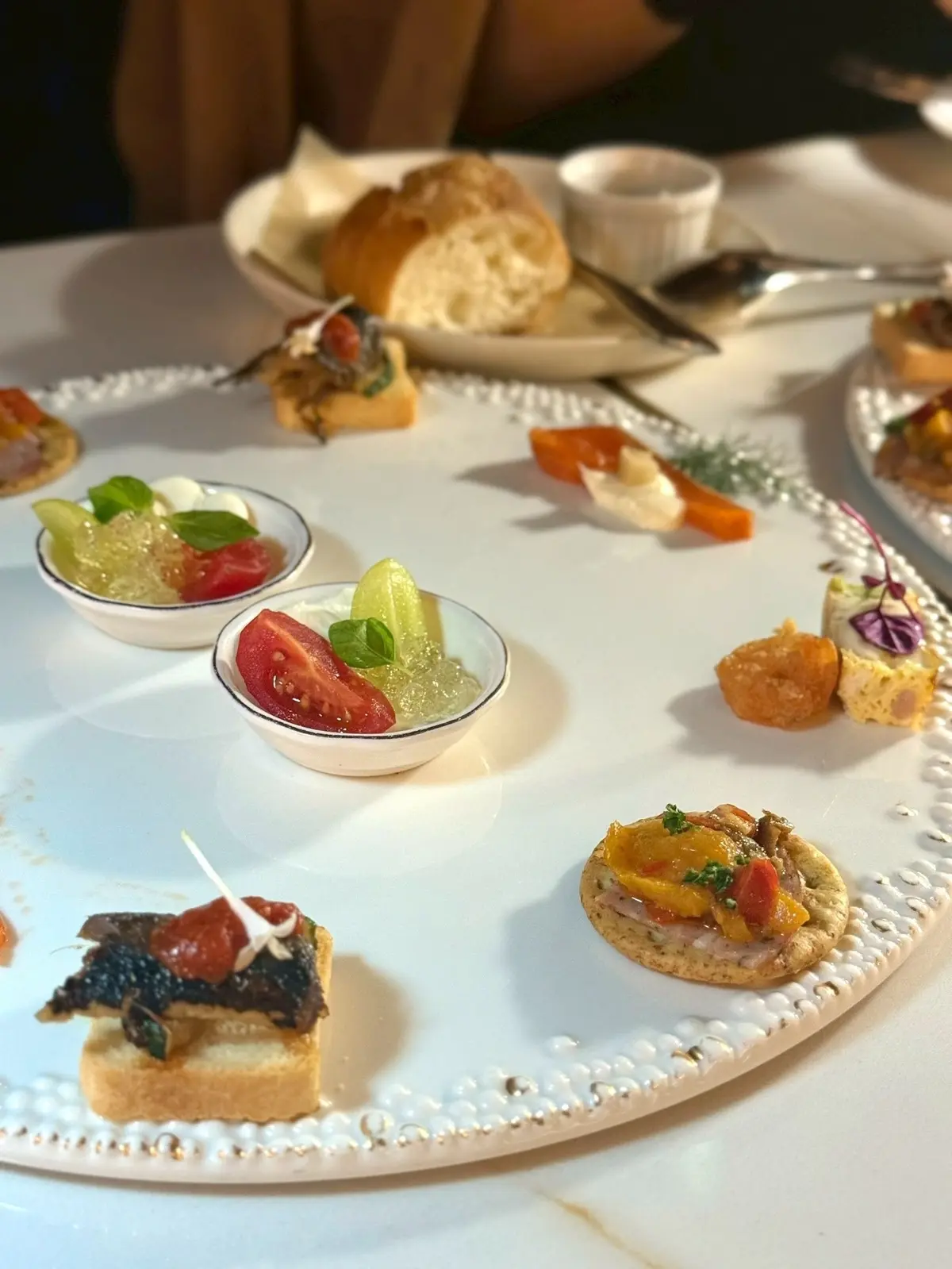 梅田ブルーバードの誕生日ディナーコースの美味しいイタリアン料理　白いテーブルに、トマトとキュウリのゼリー、パン、チーズ、フルーツ、クラッカーなどの軽食が並んでいる