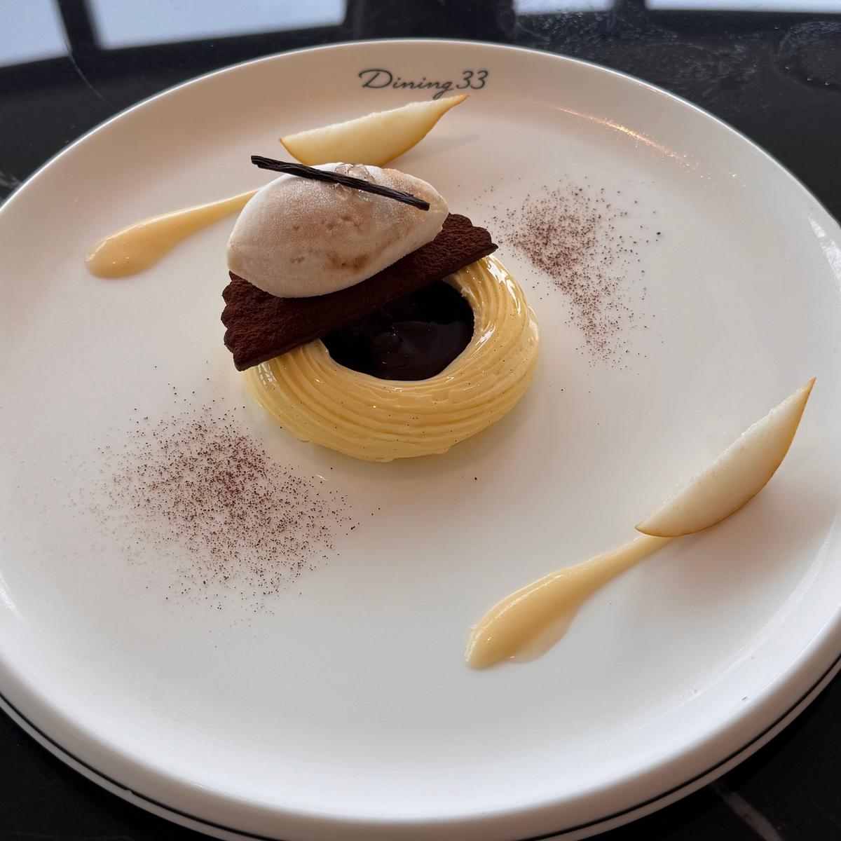 白磁の皿に盛り付けられたデザート。中央にバニラ風味のクリーム、ダークチョコレート、アイスクリームが配置。皿にはキャラメルソースとココアパウダーが散らされ、Dining 33のロゴが中央に刻印されている。
