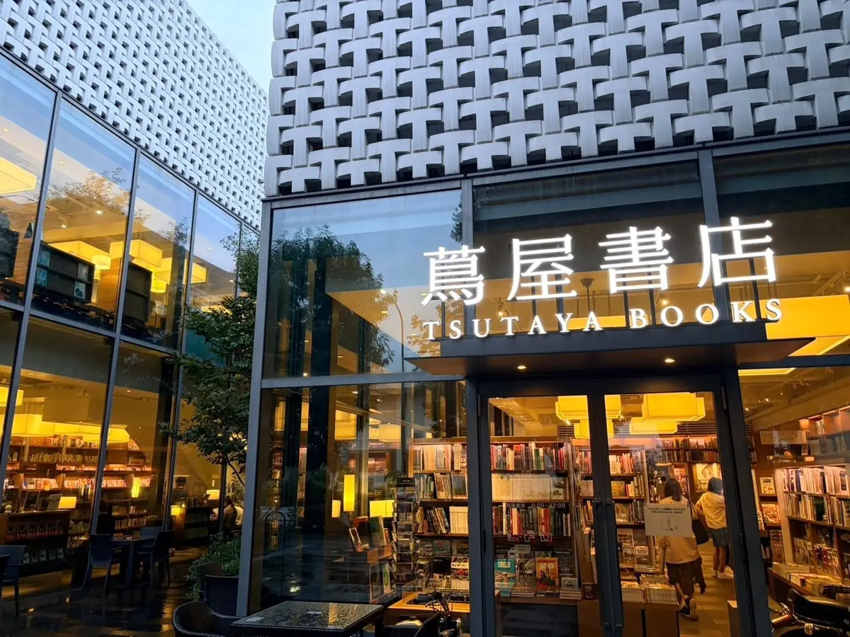 TSUTAYA BOOKSの店舗外観。全面ガラス張りの建物で、入り口には自動ドア。窓からは本棚が並ぶ様子が見え、温かい光が灯っている。建物の外観は白とグレーを基調としたモダンなデザイン。