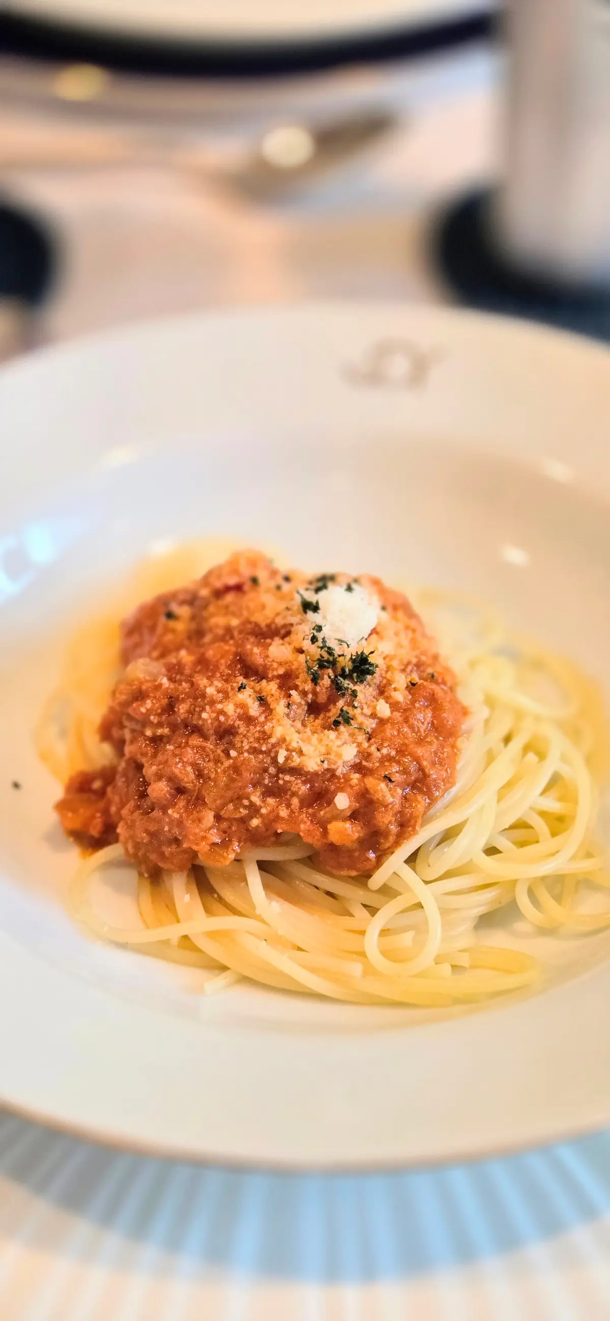 白磁の皿に盛り付けられたスパゲッティとミートソースの肉団子。肉団子にはチーズとハーブが散らされている。背景にはキッチン用品がぼやけて写っている。