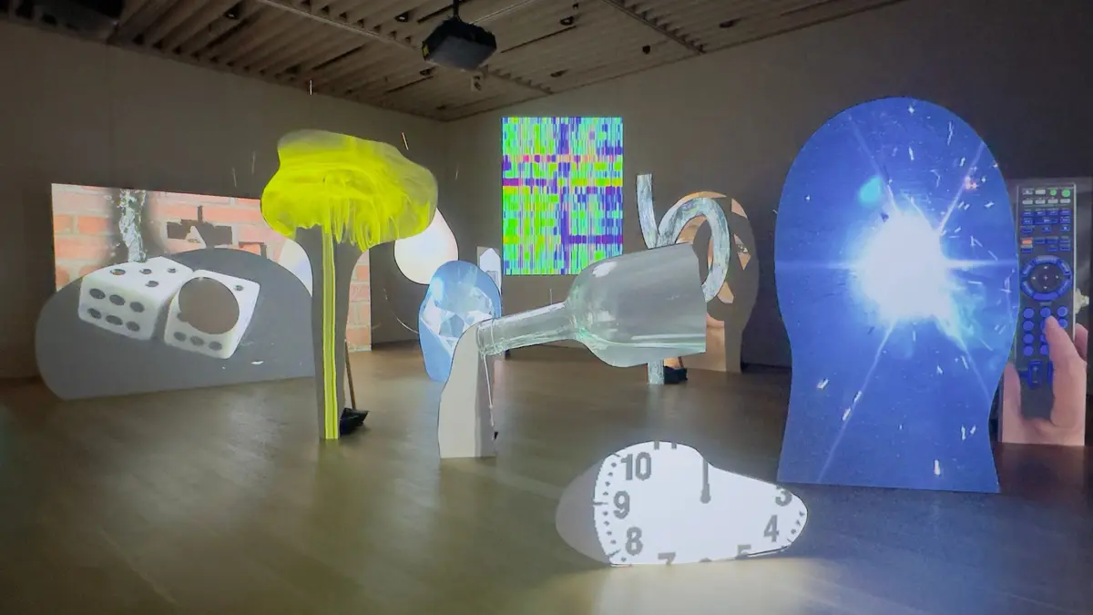 展示室に設置された、様々なモチーフが描かれた白い板が並ぶアート作品。サイコロ、ワインボトル、テレビのノイズ、リモコンなどがカラフルな光で照らされている。