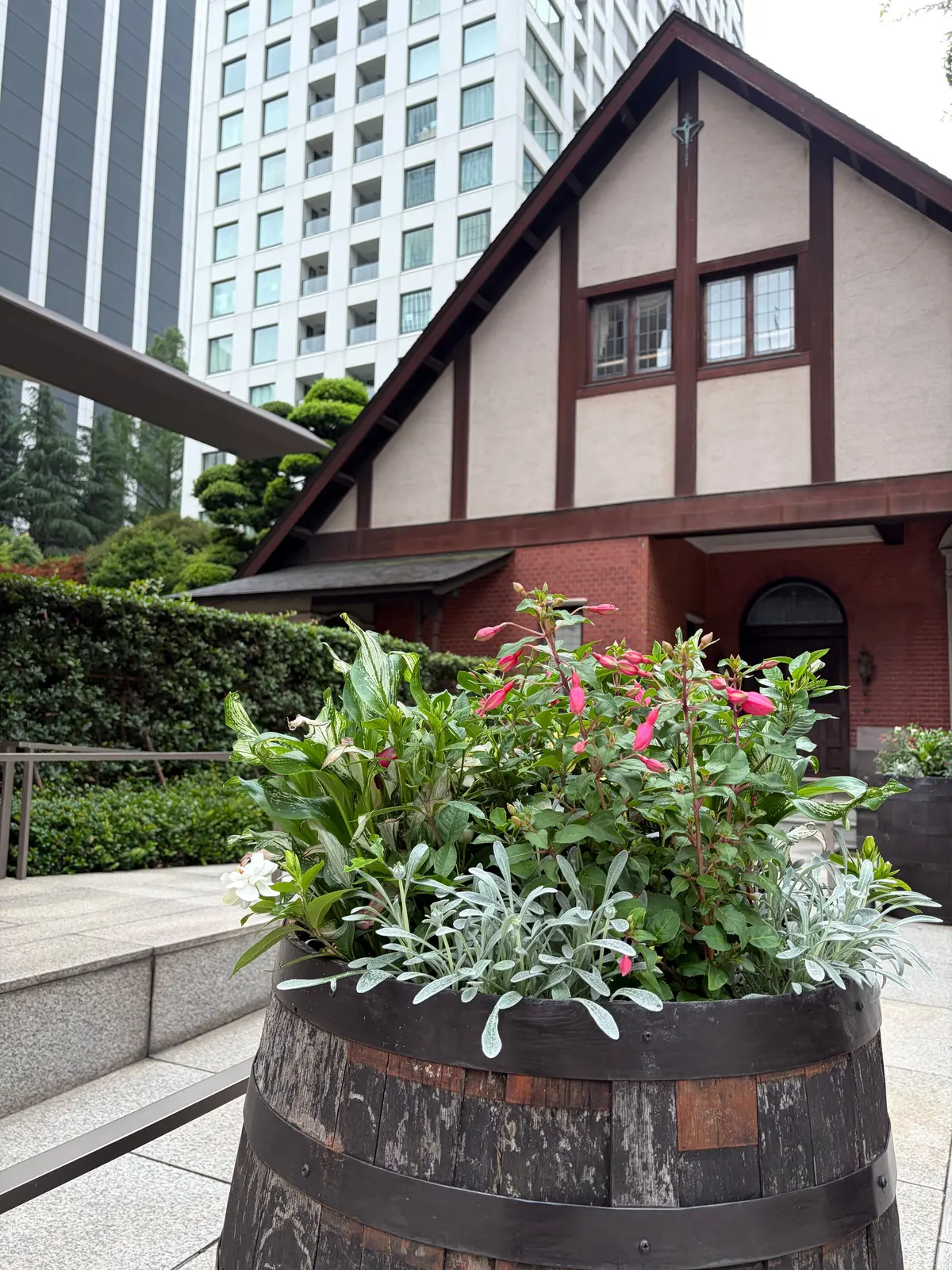 木製の樽に白と赤の花が咲く、庭のプランター。後ろには登録有形文化財に指定された西洋館が