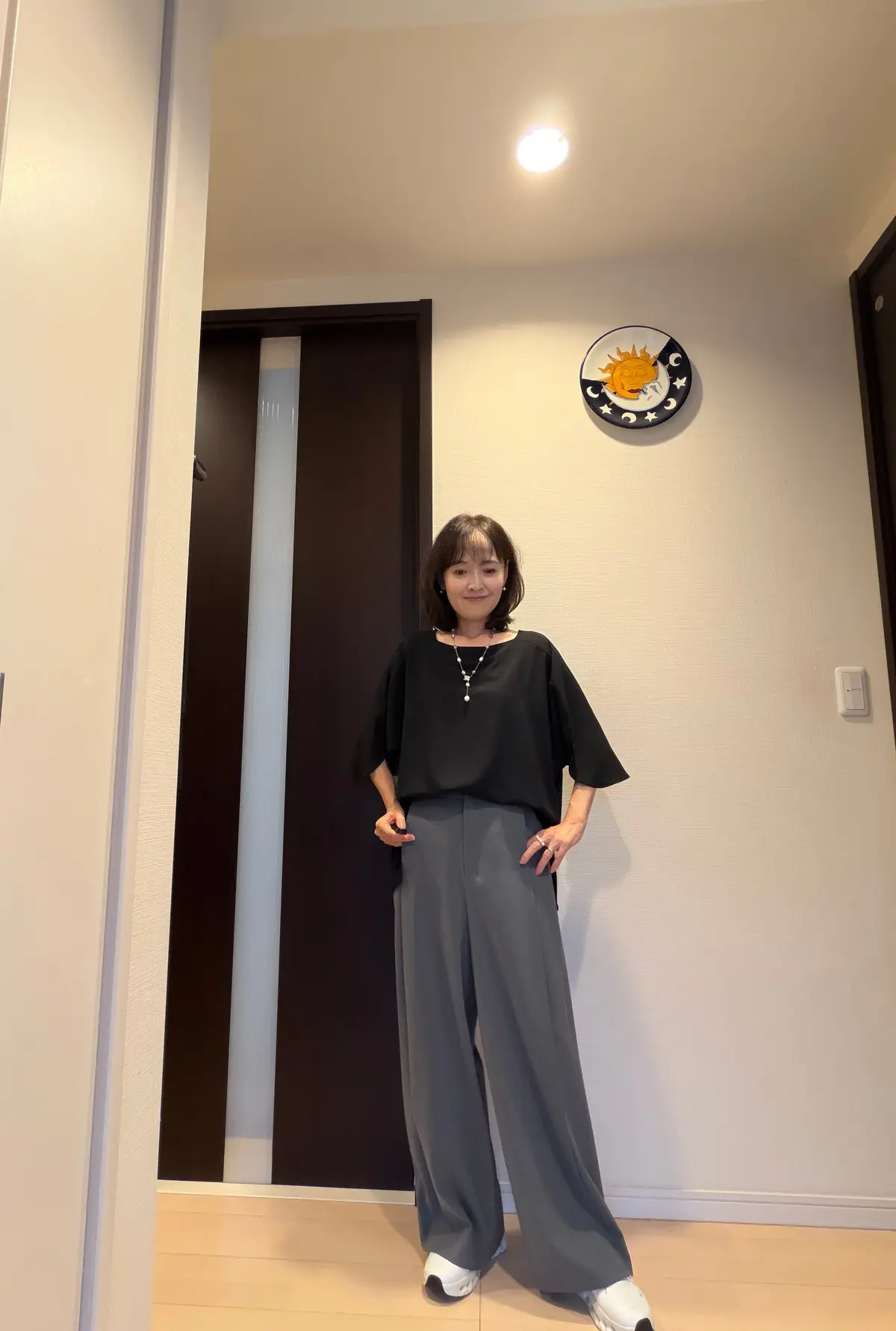 黒いカットソーとグレーのワイドパンツを着用した女性が立っている全身写真。