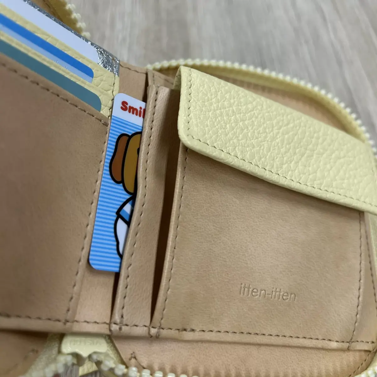 黄色のレザーの二つ折り財布。カードスロットに複数のカードが挿入されており、そのうちの一つに「Smile」と書かれたカードが見える。財布の内側には「itten-itten」のロゴが刻印されている。