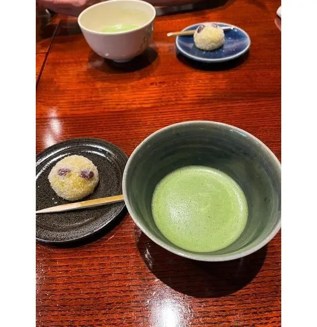木製テーブルに、緑茶の入ったグレーカップと、2つの和菓子が乗った黒いプレートが置かれている