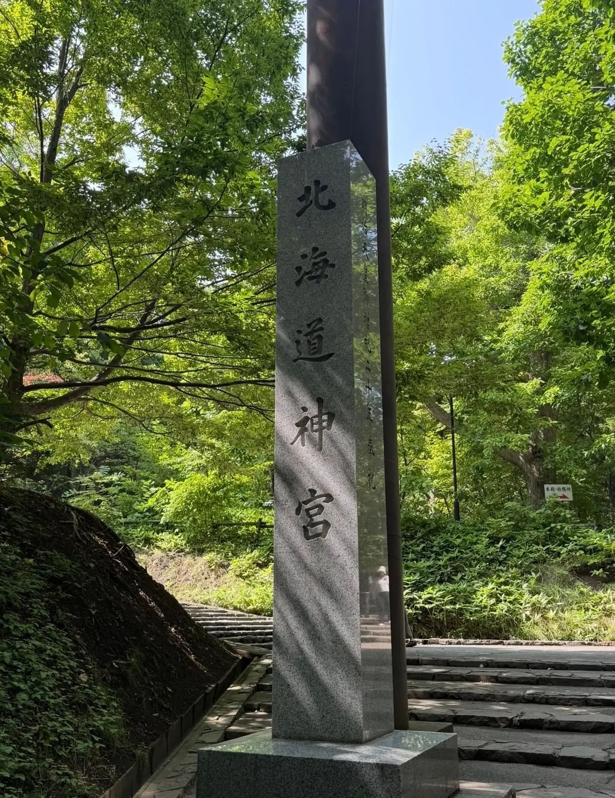 緑豊かな木々に囲まれた石碑。中央に「北方道神宮」と墨書された石碑が設置され、その前には石段が続く。