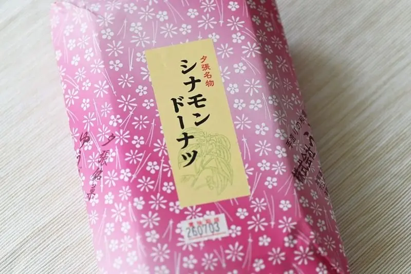 ピンクの包装紙に白い小花模様が散りばめられ、黄色のラベルが中央に貼り付けられた和菓子。ラベルには「シナモンドーナツ」の文字が書かれています。
