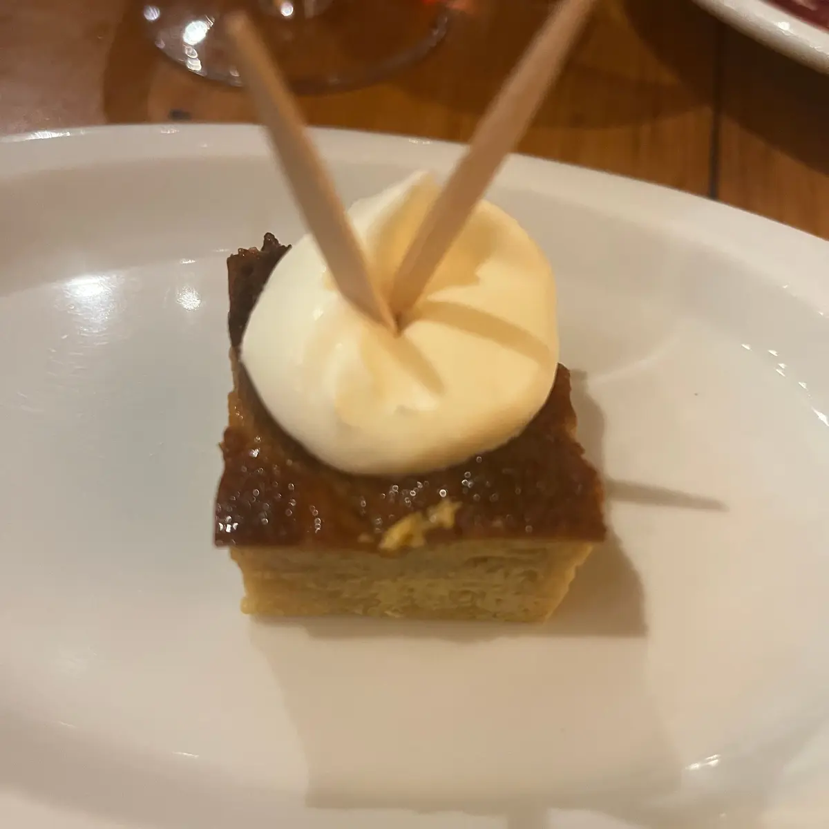 白い皿に盛り付けられた、四角いチョコレートケーキ。表面にはキャラメルクリームが丸く乗っており、竹串が刺さっている。