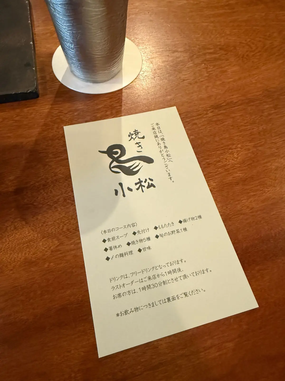 大阪・福島の人気焼き鳥店「焼き鳥 小松」でいただいた焼き鳥コース。木目調のテーブルに置かれた、手書き風のイラストと文字が印刷されたメニュー。タイトルは「焼きたて 小松」とあり、コース内容や注意事項が記載されている。上部には、白い背景に黒い線で描かれた鳥のイラストがある。