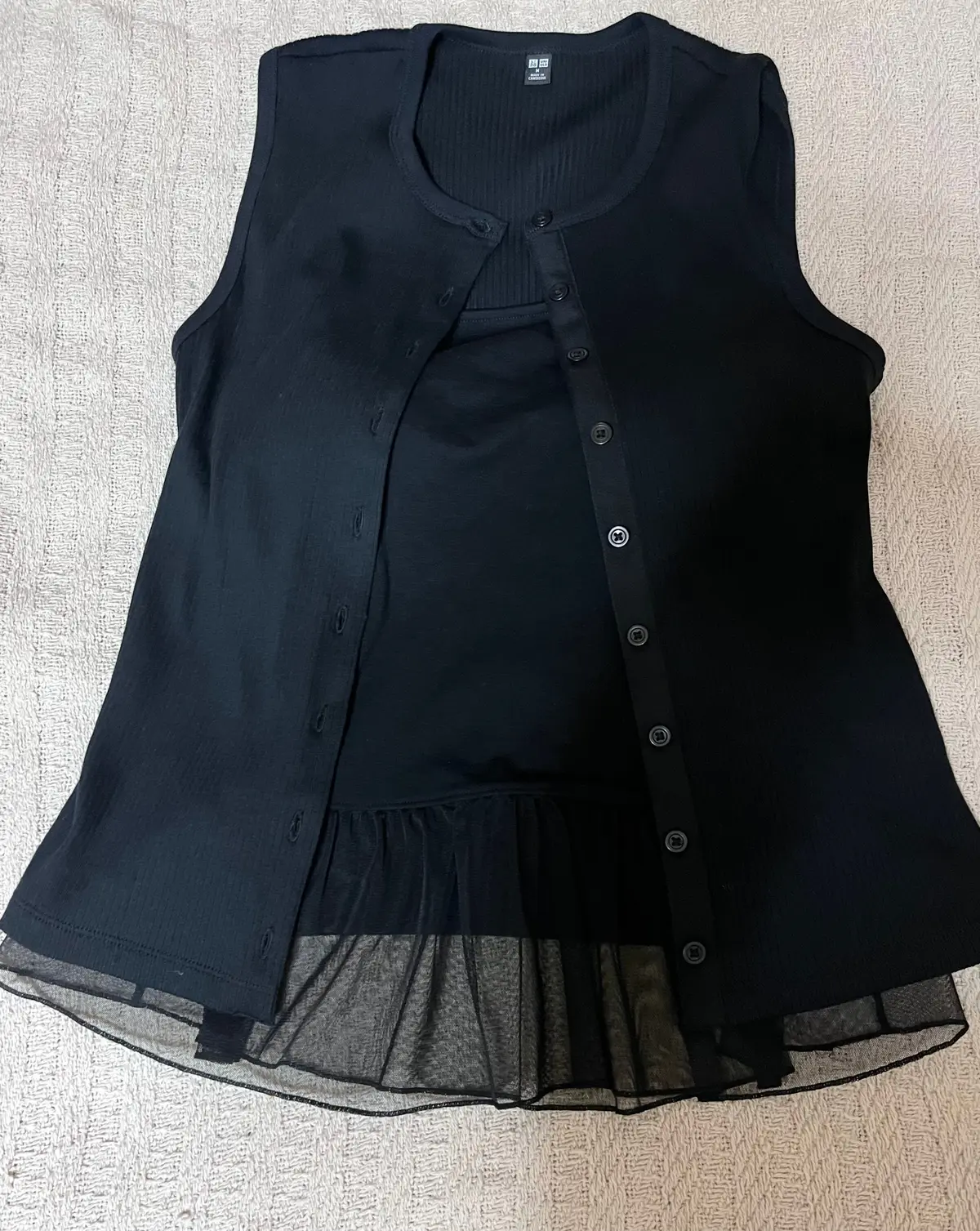 黒い2点セットアップ。タンクトップとフリル付きの半袖ブラウス。ボタンで装飾され、裾にはチュール生地が施されている。