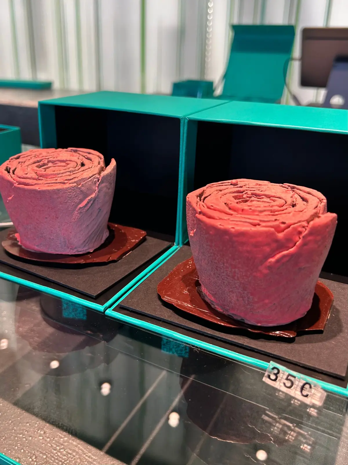 緑の展示ケースに、ピンクと赤の円筒形のオブジェクトが2つ展示されている。各オブジェクトは茶色の台座の上に置かれている。