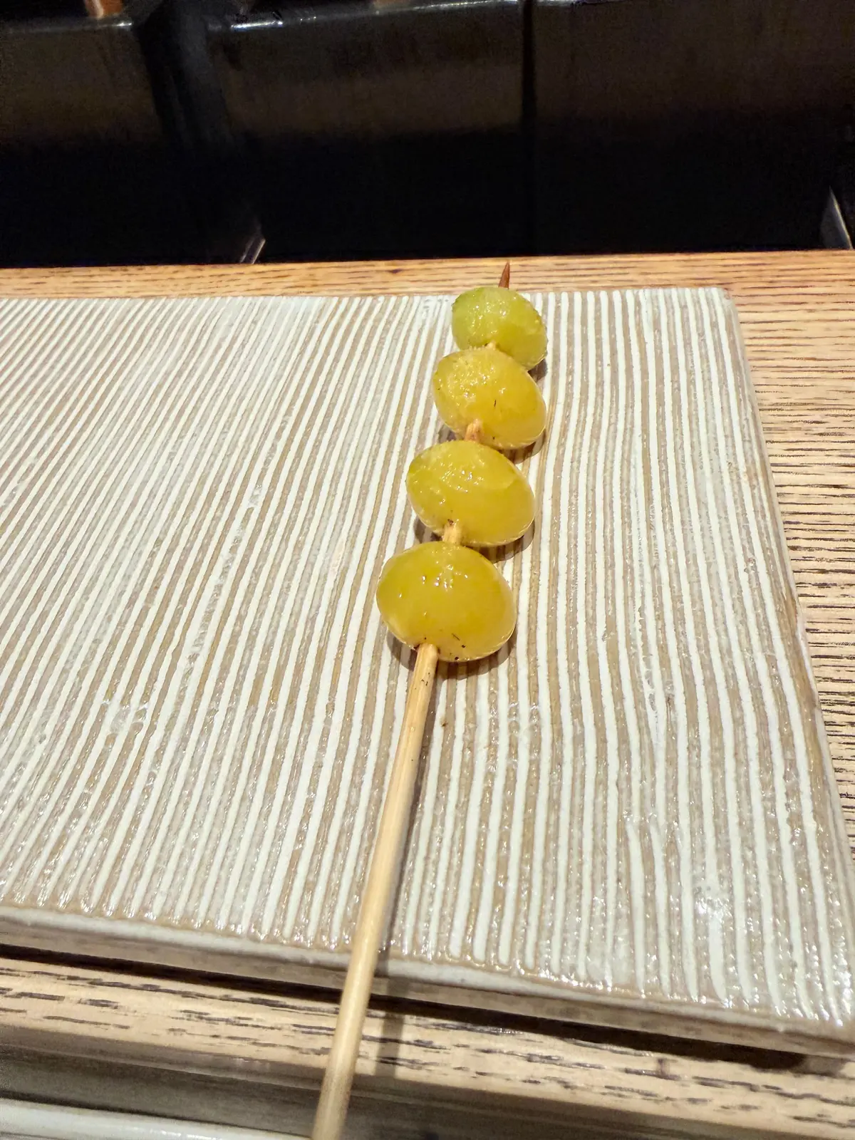 木の棒に刺さった黄色の果物4個が、縞模様の白いプレートに並んでいる