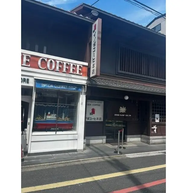 INODA COFFEE SHOPの店外観。赤と白の看板とガラス窓があり、店内にはコーヒーカップとテーブルが見える。隣にはINODA COFFEEの看板付きの建物がある。