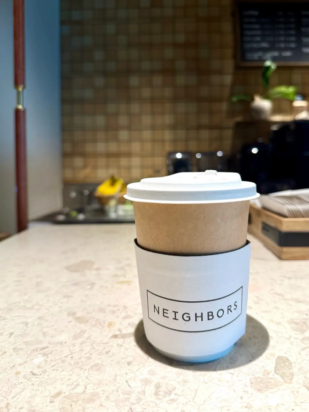 １Hotel Tokyo ３８階　カフェ「Neighbors Café」、紙カップに「NEIGHBORS」の文字入りホルダー付きコーヒー、キッチンカウンターに置かれています