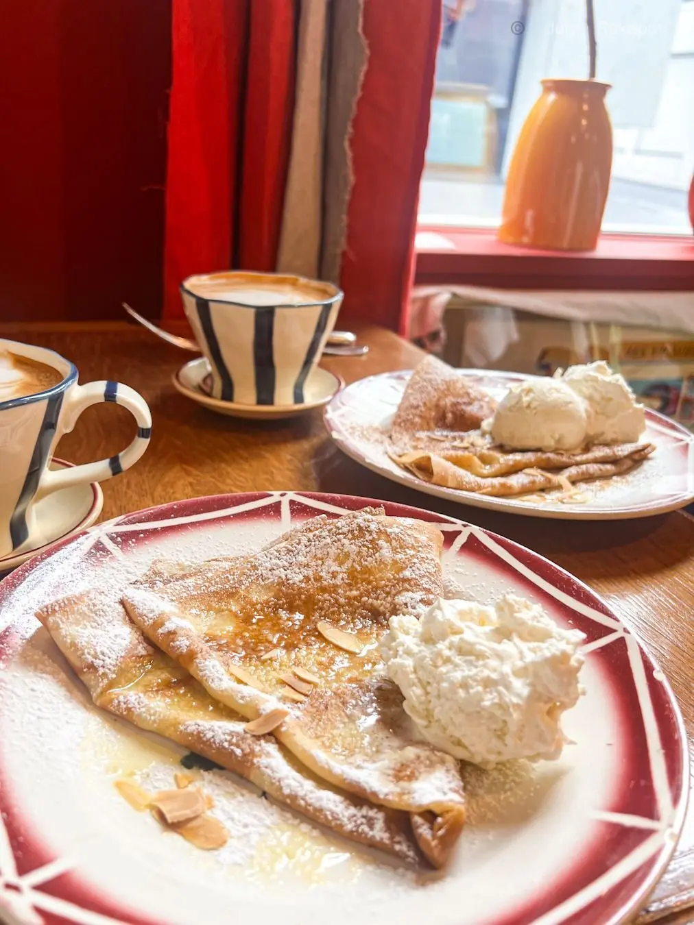 木のテーブルに、粉砂糖をまぶしたパンケーキとアイスクリームが並ぶ。白と青のストライプ模様のカップにコーヒーも置かれている。