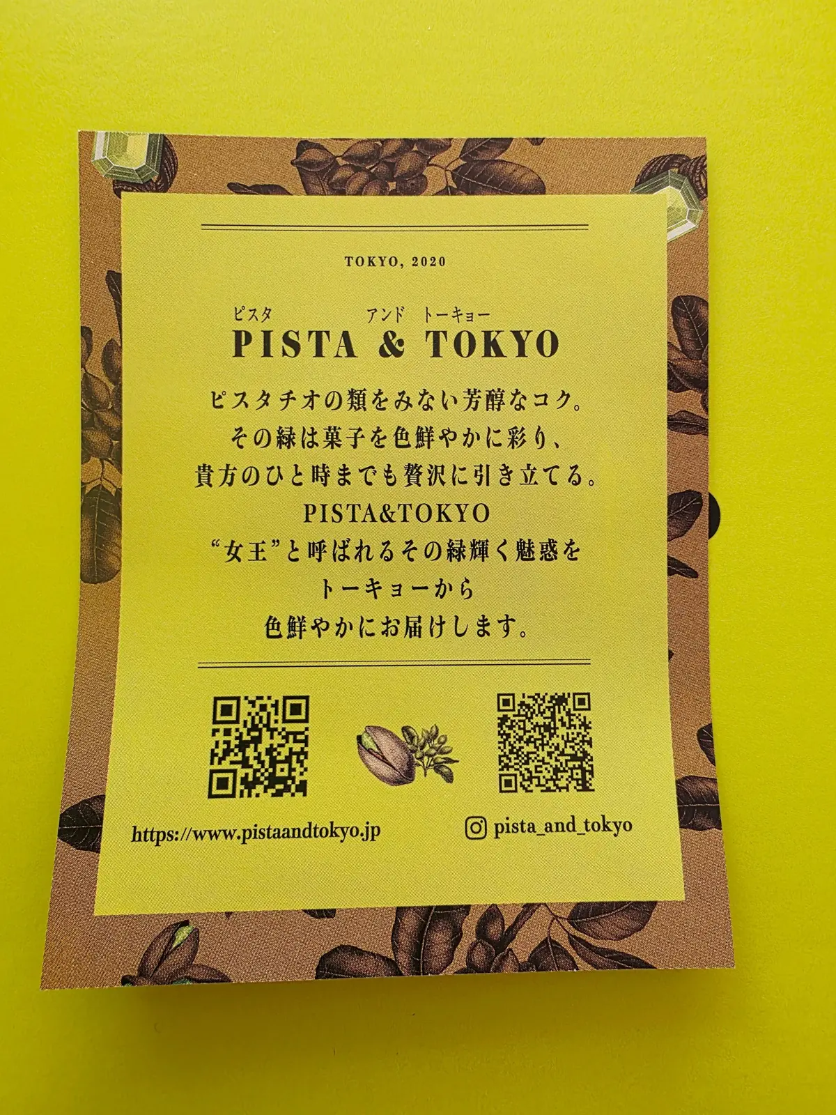 ピスタチオと東京のロゴが入ったカード。背景にはピスタチオの実が散りばめられ、中央に日本語でブランド紹介文とウェブサイト、InstagramへのQRコードが配置されている。